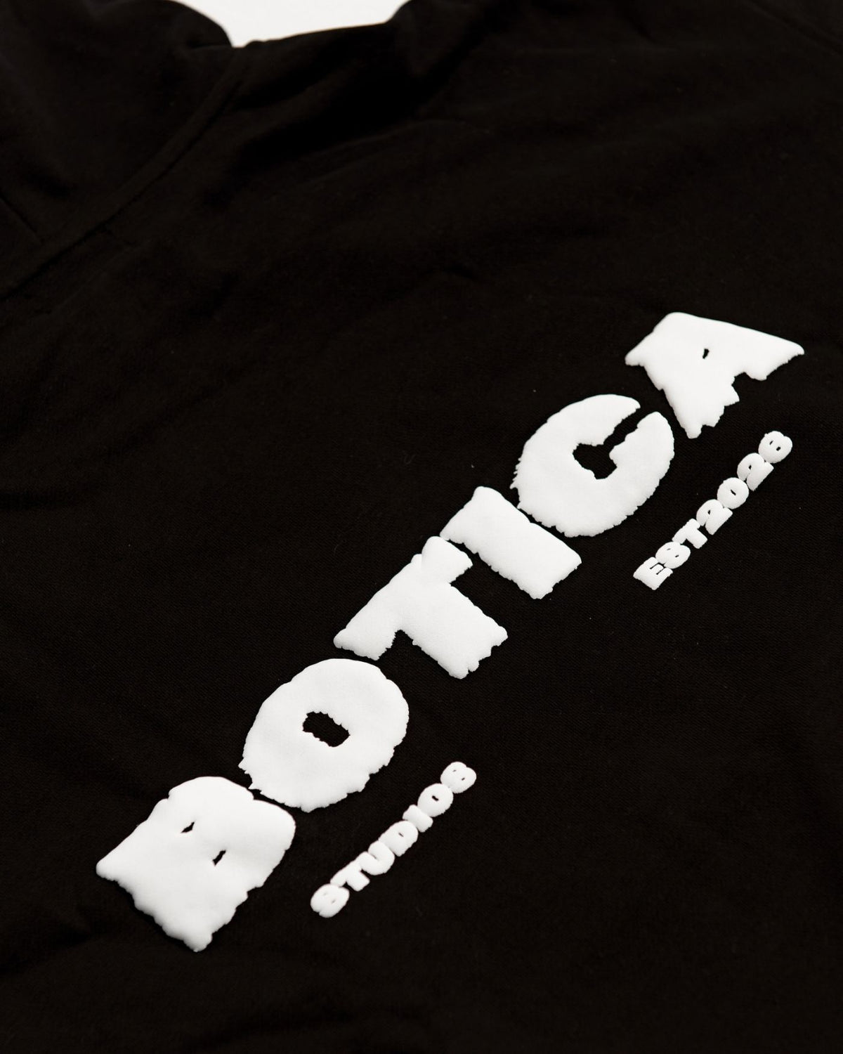 Close-up of the raised puff print BOTICA STUDIOS back graphic on black fabric