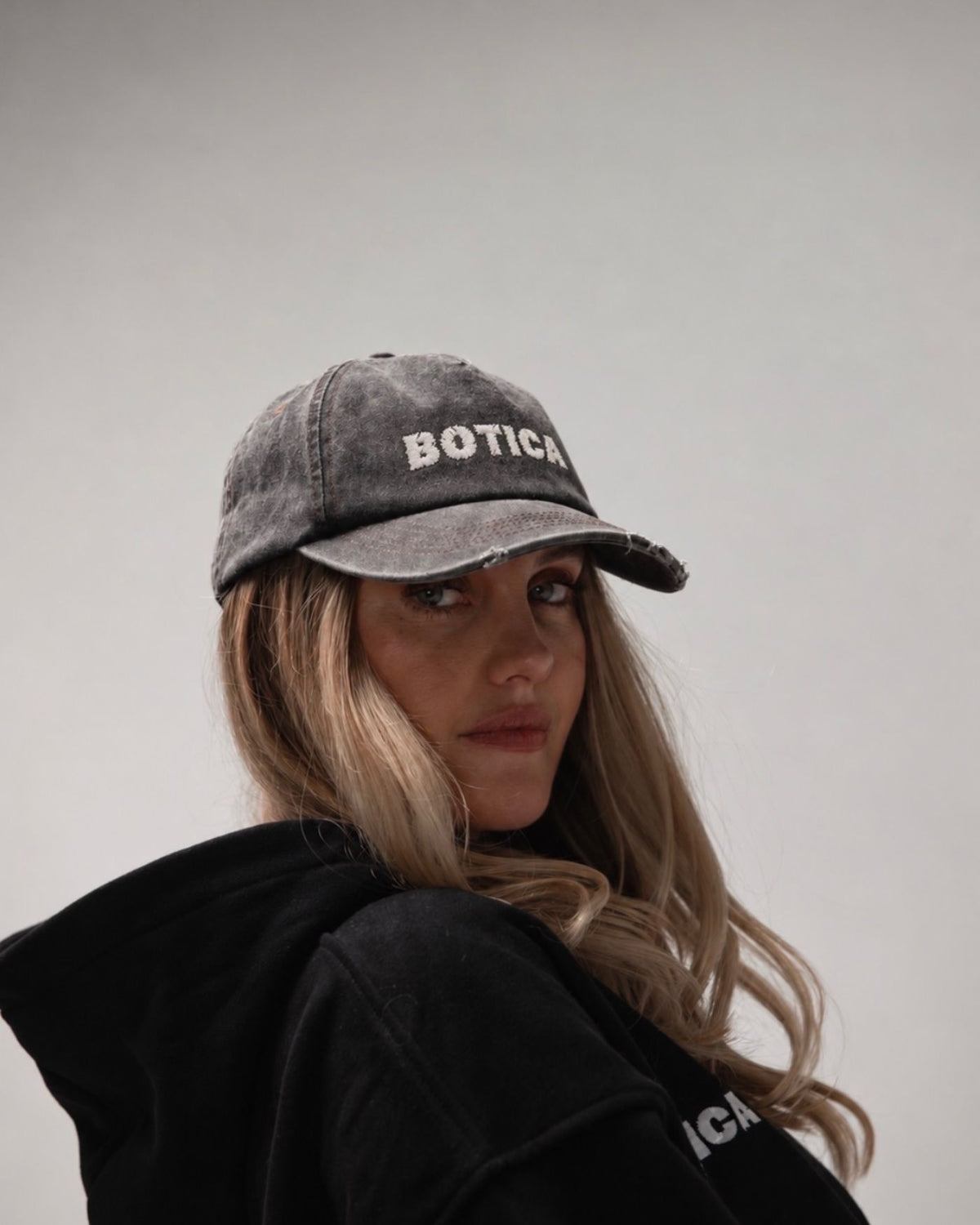 Model wearing The Logo Cap in washed black with a black hoodie, looking over their shoulder